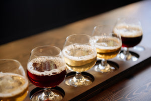 Row of beer glasses with different types of beer on a metal tray.
