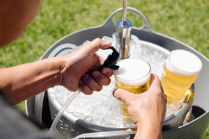 Person pouring beer from a tap into two glasses in an outdoor setting.