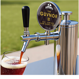Beer tap labeled 'The Guvnor III' dispensing beer into a glass with a blurred green background.
